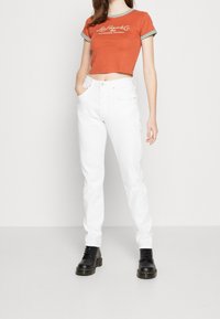 Camiseta cortada color óxido con rayas verdes en el collar, combinada con unos vaqueros blancos de tiro alto y botas negras con cordones.
