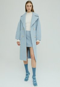 Helles blaues Karomuster-Mantel mit einem breiten Kragen, doppelreihigen Knöpfen und einem hohen Schlitz bis zum Oberschenkel, kombiniert mit einem passenden Rock und blauen Socken.