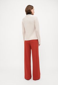 Beige strikkegenser med kort hem, kombinert med brede røde bukser. Designet har en ribbestruktur og klassisk krage.