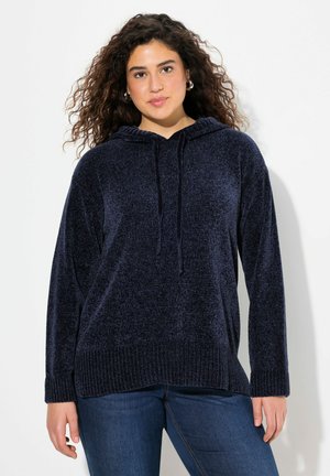 Sweat à capuche bleu marine en tissu doux et texturé, avec un cordon de serrage à la capuche, des poignets et un ourlet côtelés. Porté avec un jean en denim.