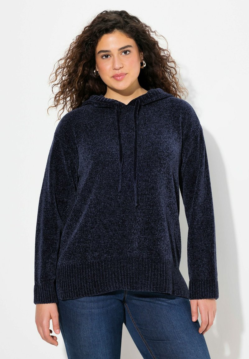 Felpa blu navy realizzata in morbido tessuto testurizzato, con cappuccio regolabile, polsini e orlo a coste. Indossata con jeans di denim.