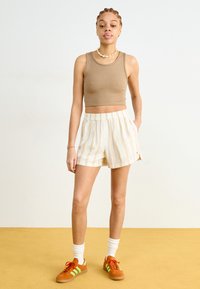 Hnědý žebrovaný crop top, bílé šortky se žlutými pruhy, oranžové tenisky se zelenými pruhy a bílé sportovní ponožky.