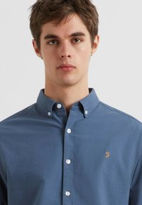 Blauwe button-up shirt van katoen met een klein geborduurd logo op de borst, voorzien van een klassieke kraag en witte knopen.