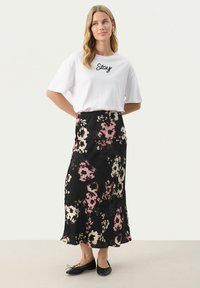 T-shirt blanc surdimensionné avec "Stay" en cursive noire, associé à une jupe midi noire à fleurs avec des motifs roses et crème et un ourlet évasé.
