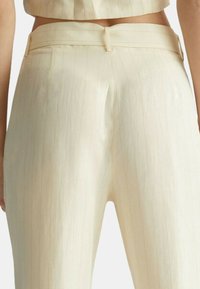 Pantaloni color crema con texture a righe, dotati di vita aderente e design a gamba dritta. Senza hardware o accenti visibili.