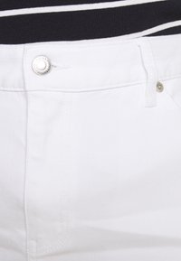 Close-up of white denim jeans waist with silver button and belt loop, worn with black and white striped top.