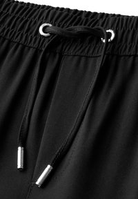 Shorts en tissu noir avec une taille élastique, un cordon de serrage avec des éléments en métal argenté, et un détail de surface texturé.