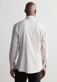 Cămașă lungă cu mânecă, de culoare bej deschis, cu guler ascuțit, manșete cu nasturi și tiv curbat. Fabricată dintr-un material moale, având o textură netedă.