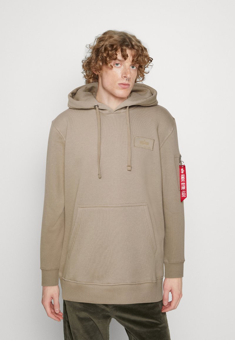 Beženi kapućo s džepom na kenguru, rebrastim manžetama in teksturirano oznako. Ima rdečo nalepko na levem rokavu.