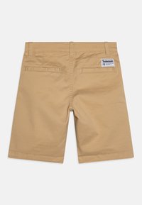 Pantaloni corti in cotone beige con vestibilità dritta, dotati di due tasche posteriori e etichetta Timberland sulla vita. Texture liscia e design classico.
