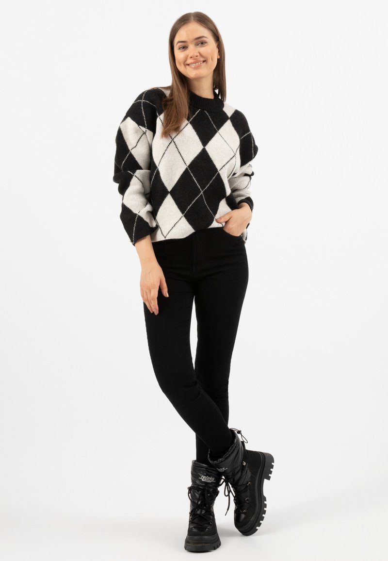 Pull en argile noir et blanc avec un col rond, associé à un jean skinny noir et des bottes montantes noires à lacets.