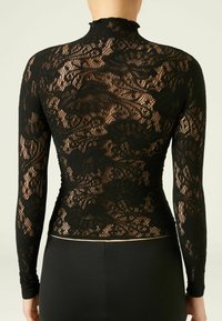 Czarny koronkowy top z długimi rękawami, z wysokim kołnierzem i kwiatowymi wzorami. Tkanina jest półprzezroczysta o teksturowanym, misternym wzorze.