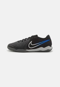 Černé nízké sportovní boty Nike s šedou podrážkou, modrým a bílým logem swoosh a černým síťovinovým svrškem na bílém pozadí.