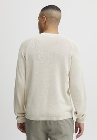Hellbeige gestrickter Pullover mit einem gerippten Saum und Bündchen. Er hat einen Rundhalsausschnitt und Raglanärmel, die einen strukturierten Stoff präsentieren.
