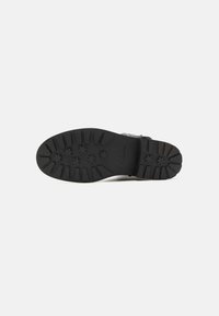 Suela de zapato de goma negra con patrón de tracción estriado y logo de la marca. Presenta un diseño plano y duradero, adecuado para diversas superficies.