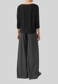 Czarna bluzka z rękawami do połowy ramienia w połączeniu z szarymi spodniami o szerokich nogawkach. Materiał bluzki jest miękki, a spodnie mają gładką fakturę.