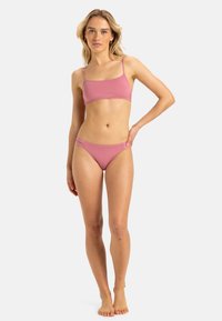 Różowy zestaw bikini z minimalnym biustonoszem na cienkich ramiączkach i niskimi majtkami, wykonany z gładkiej elastycznej tkaniny.