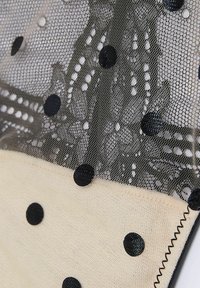 Zbliżenie beżowego materiału w czarne kropki oraz warstwowej czarnej koronki z kwiatowymi wzorami i cienką siateczką na wierzchu.