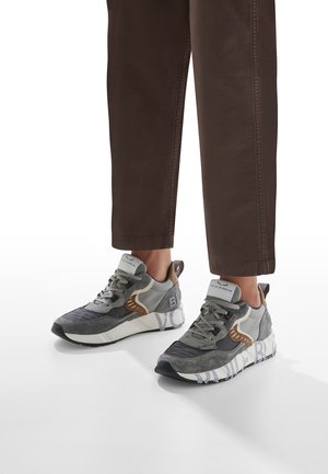 Graue und beige Sneakers mit strukturiertem Obermaterial, aus Mesh- und Wildleder-Materialien, dicker Sohle und sichtbarem Branding an der Seite.