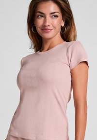 Camiseta de manga corta rosa claro, hecha de tejido de punto texturizado, con rayas verticales acanaladas y detalles de ojales delicados.