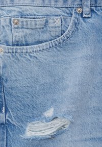 Tissu en denim bleu clair avec une poche avant, un rivet argenté et une zone usée avec des bords effilochés.