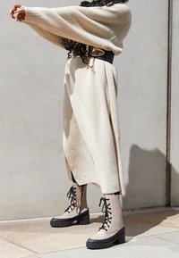 Un pull beige à côtes associé à une jupe beige fluide. Des bottes à lacets chunky beige et noires avec une semelle plateforme et une finition texturée.