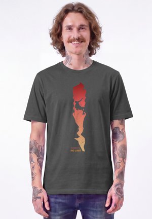Homme avec des tatouages sourit en portant un t-shirt noir montrant un grimpeur escaladant une falaise avec le texte "There's no limit."