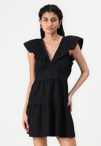 Vestido curto preto com um decote V profundo, mangas com babados e cintura franzida. Apresenta uma silhueta em A e um tecido texturizado.