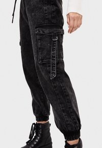 Svarta denim cargo byxor med sidofickor och elastiska ärmslut. Tyget har en blekt struktur och en dragsko i midjan.