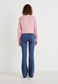Pink knitted sweater with ribbed cuffs, paired with blue flared jeans featuring contrasting white stitching. Model wearing white sneakers.