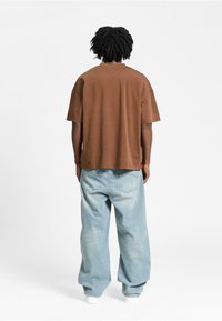 Brun kortærmet T-shirt med lige snit, parret med lyseblå, løstsiddende denim jeans og hvide sneakers.