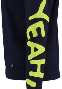 Maglietta a maniche lunghe blu navy con grande testo giallo brillante che legge "YEAH!" sul braccio sinistro. Il tessuto appare liscia, con una vestibilità comoda.