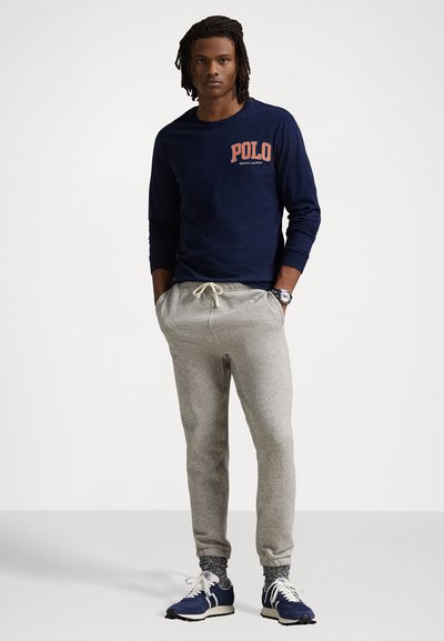 Námornícky tričko s dlhým rukávom s nápisom "POLO", v kombinácii so svetlosivými teplákmi a námorníckymi športovými topánkami. Neformálny, voľný strih.