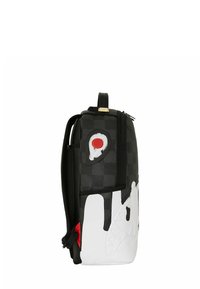 Mochila en blanco y negro con un diseño de cara de tiburón en rojo y blanco, patrón a cuadros negro y un asa superior.