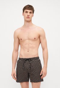 Fekete úszónadrág geometrikus mintával narancssárgában és fehérben, rugalmas derékkal és zsinóros részlettel.