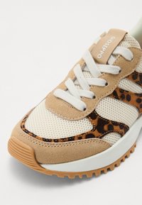 Baskets marron et beige avec une tige en mesh, des accents en suède, des détails en imprimé léopard, des lacets blancs et une semelle en caoutchouc texturée.