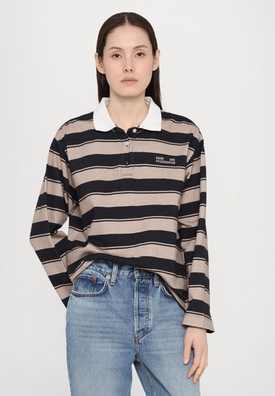 Svart og beige stripete long-sleeve polo med hvit krage, med knappelukking og logo-detalj på brystet, iført blå jeans.