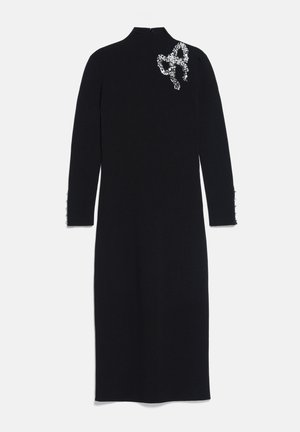 Robe midi noire à manches longues avec col haut et nœud décoratif en strass sur l'épaule gauche.