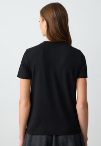 Zwart T-shirt met korte mouwen, een geribbelde textuur, ronde halslijn en een aansluitend ontwerp, gezien vanuit de achterkant, met een gladde stofafwerking.