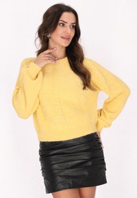 Pulover galben tricotat cu țesătură texturată �și aplicații din perle, asociat cu o fustă mini din piele neagră, ajustată.