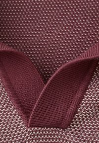 Plano detalle de tela de punto en granate y blanco con puños de canalé granate doblados y superpuestos encima.