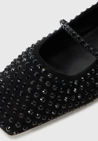 Ballerines en daim noir avec un bout arrondi et des strass noirs décoratifs disposés en motif sur la surface.