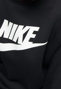 Černá mikina s výrazným bílým logem „NIKE“ a výrazným efektním znakem swoosh na přední straně. Měkká textura látky.