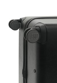 Svart hård resväska med två svarta hjul m ärkta "LEGO", en slät dragkedja och en texturerad yta. Ren, modern design.