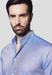 Jasnoniebieska koszula zapinana na guziki o miękkiej teksturze, z kołnierzykiem typu stójka i subtelnym połyskiem, z widocznymi szwami i guzikami.