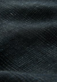 Gros plan d’un tissu texturé gris foncé avec un motif de tissage en forme de grille et de subtiles réflexions de lumière à la surface.