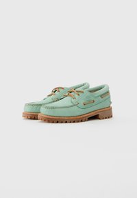 Pair of mint green leather boat shoes with tan laces and rugged brown rubber soles, placed on a neutral gray background.