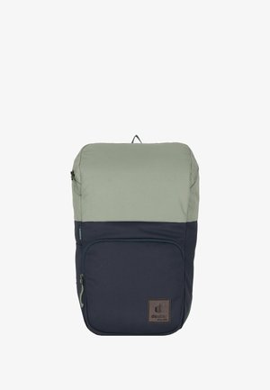 Sac à dos bicolore en vert olive et bleu marine avec une poche zippée à l'avant et un patch en cuir de la marque en bas à droite.
