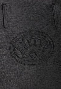 Zwarte leren tote bag met een gestructureerd oppervlak, een gegraveerd logo in het midden en twee verticale handvatten voor het dragen.