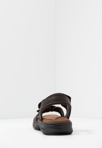 Sandal in pelle marrone con tre cinturini regolabili, soletta imbottita color beige e suola in gomma nera. Presenta dettagli di cucitura a vista.